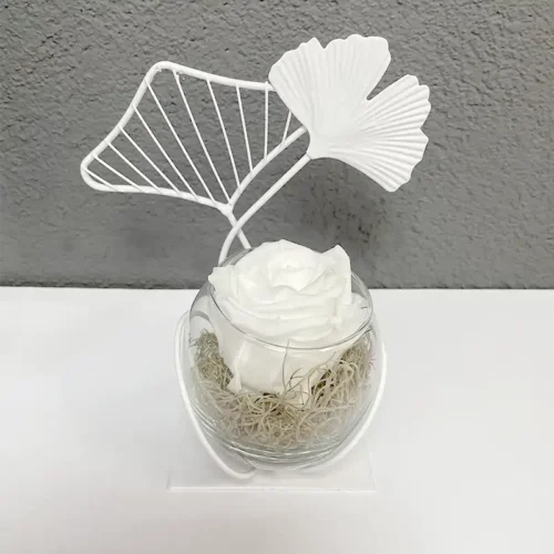 bouton de rose éternelle blanche dans un globe de verre entouré d'une décoration ginko blanche métal